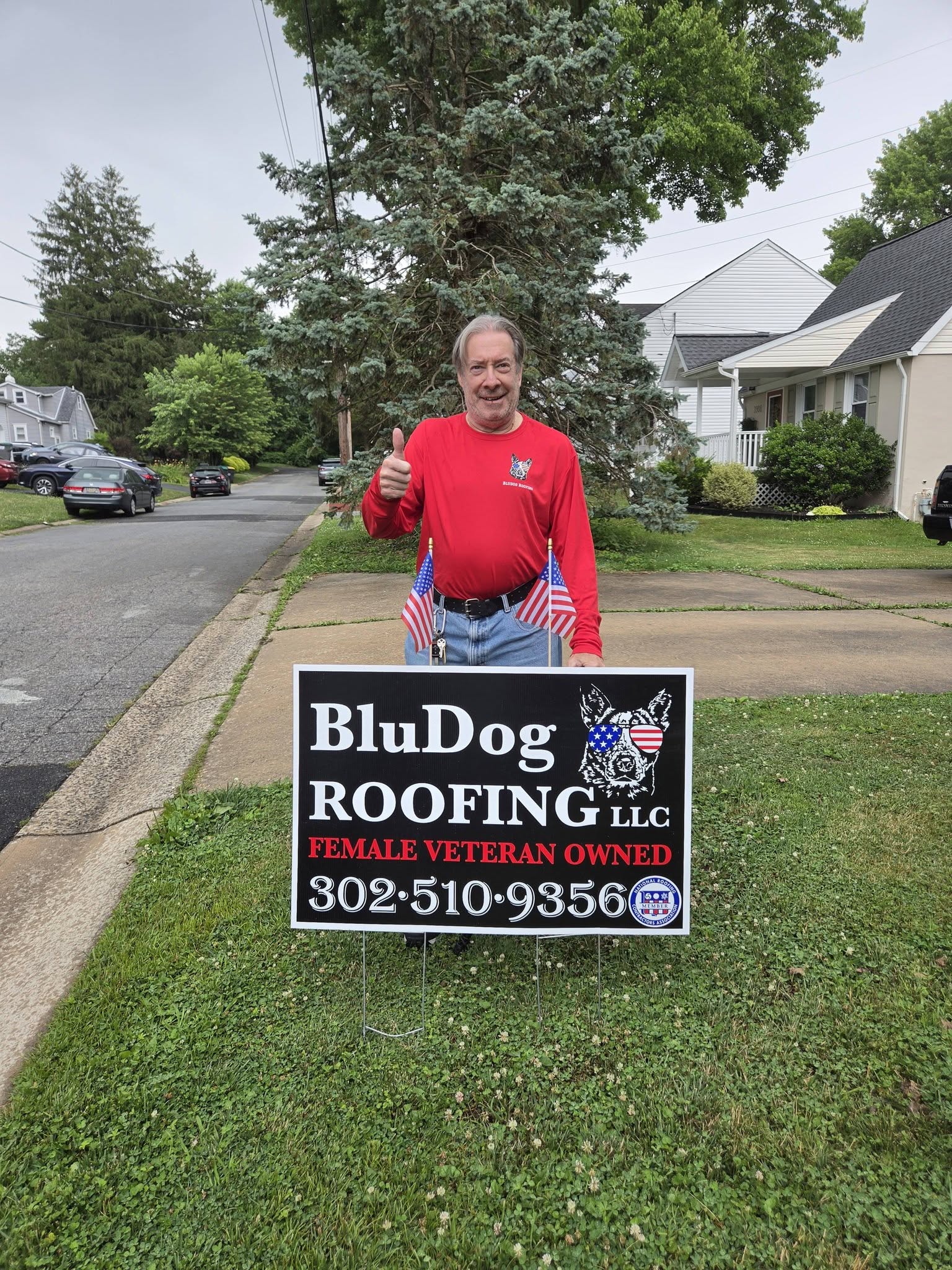 Homeowner standing next to a BluDog Roofing yard sign